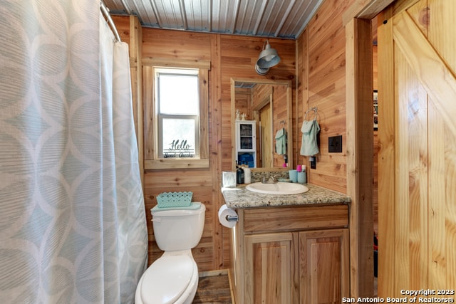 bathroom featuring wooden ceiling, vanity, toilet, and wooden walls
