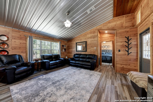 living room with hardwood / wood-style floors, wooden walls, and vaulted ceiling