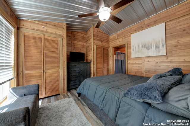 bedroom featuring lofted ceiling, wood walls, ceiling fan, and light hardwood / wood-style floors