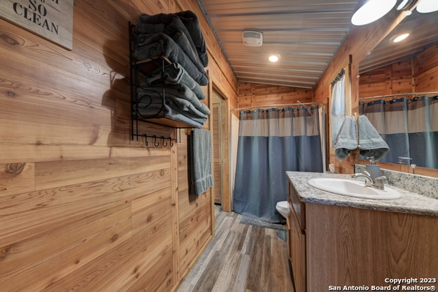 bathroom with vanity, vaulted ceiling, wood walls, hardwood / wood-style floors, and toilet