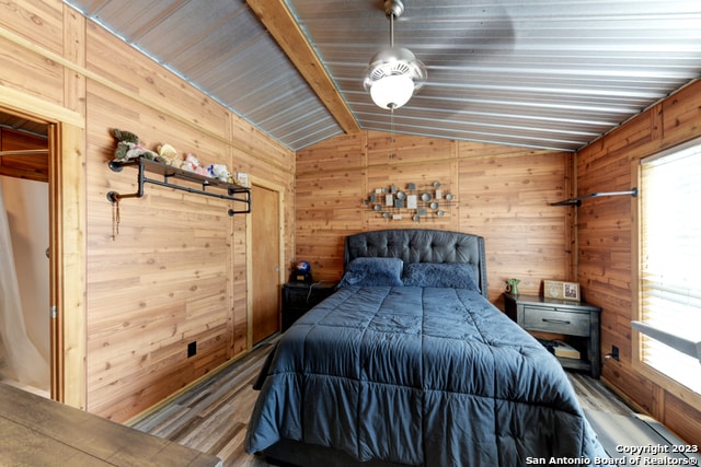unfurnished bedroom featuring multiple windows, vaulted ceiling, and wooden walls