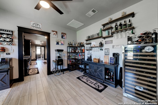interior space featuring ceiling fan, beverage cooler, indoor bar, and light wood-type flooring