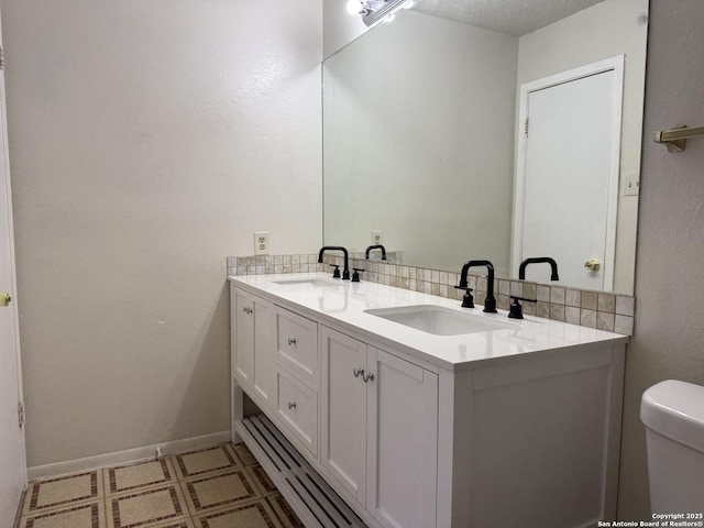 bathroom featuring double vanity, baseboards, toilet, and a sink