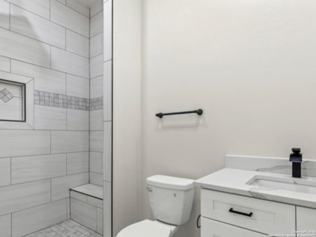 bathroom featuring tiled shower, toilet, and vanity