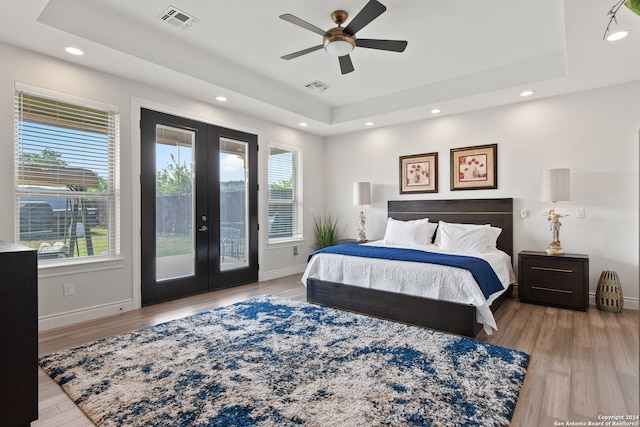 bedroom featuring a raised ceiling, french doors, access to exterior, ceiling fan, and light wood-type flooring