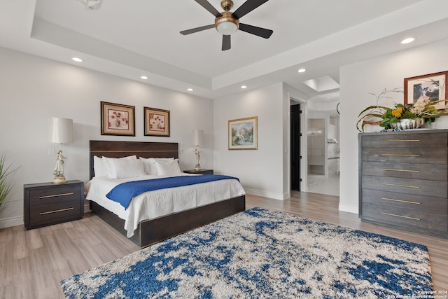 bedroom with light hardwood / wood-style flooring, ceiling fan, ensuite bathroom, and a tray ceiling