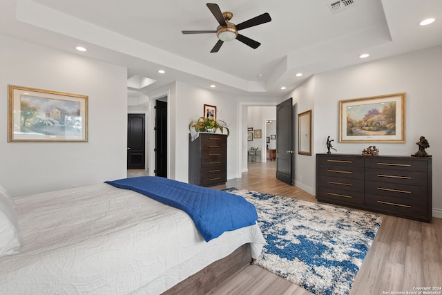 bedroom with a tray ceiling, light hardwood / wood-style flooring, and ceiling fan