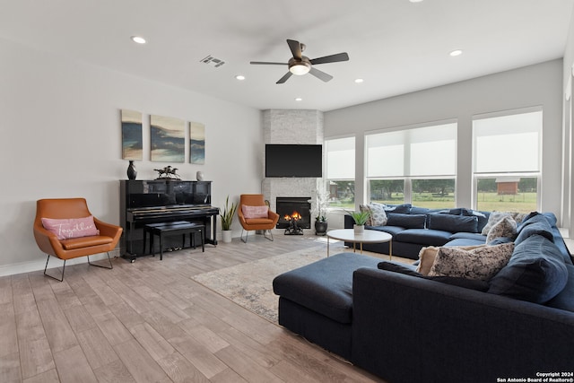 living room with ceiling fan, light hardwood / wood-style floors, and a stone fireplace