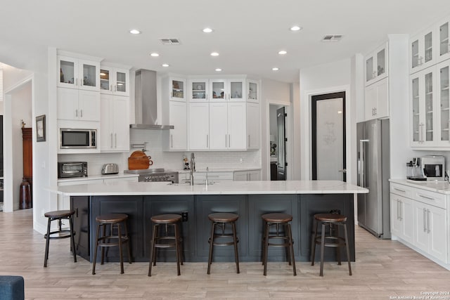 kitchen with a spacious island, stainless steel appliances, wall chimney exhaust hood, and white cabinetry