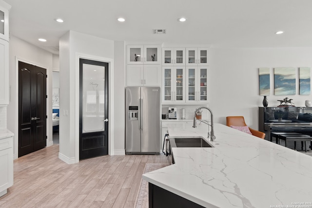 kitchen featuring high end refrigerator, light stone countertops, and white cabinets