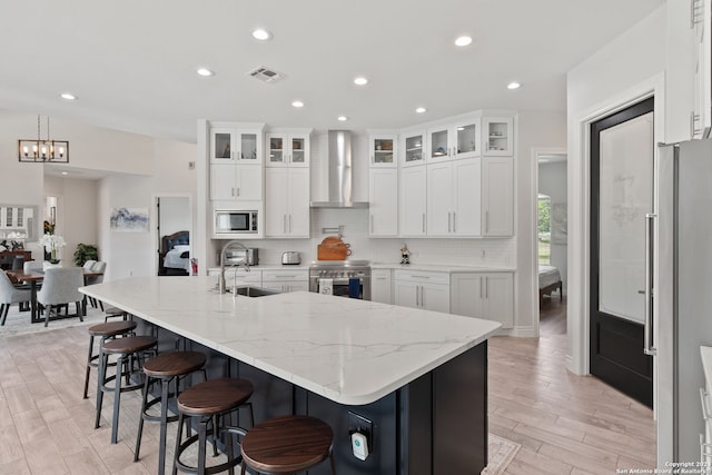 kitchen with a large island with sink, stainless steel appliances, wall chimney exhaust hood, and white cabinets