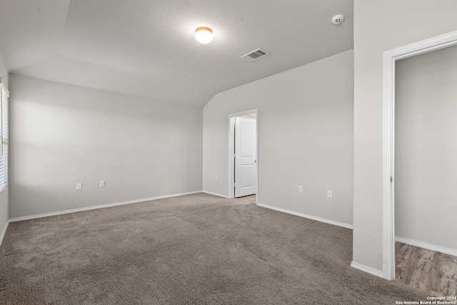 carpeted spare room featuring lofted ceiling and a textured ceiling