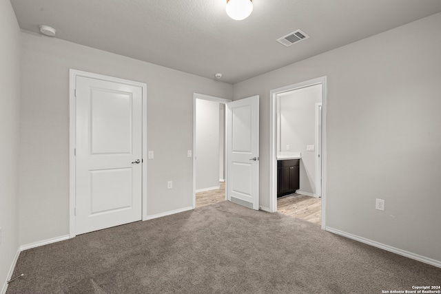 unfurnished bedroom with light colored carpet and connected bathroom