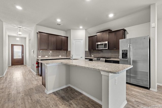 kitchen with tasteful backsplash, light hardwood / wood-style flooring, light stone countertops, appliances with stainless steel finishes, and a center island with sink