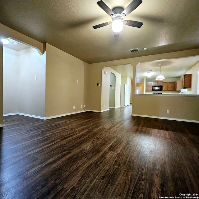 unfurnished living room with a textured ceiling, dark wood-type flooring, and ceiling fan