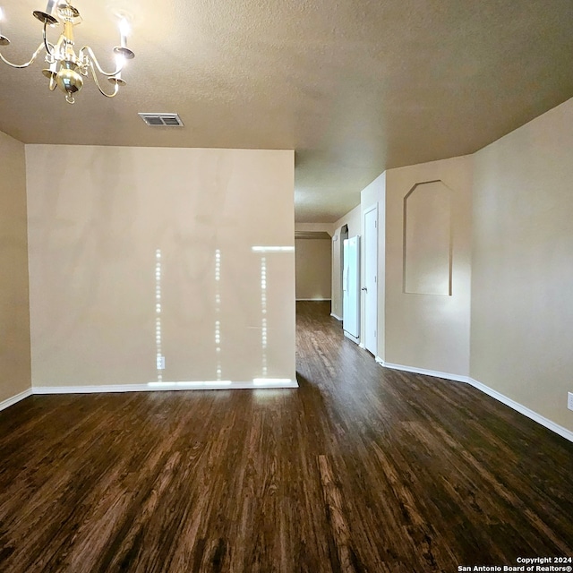 unfurnished room with dark wood-type flooring, a textured ceiling, and a chandelier