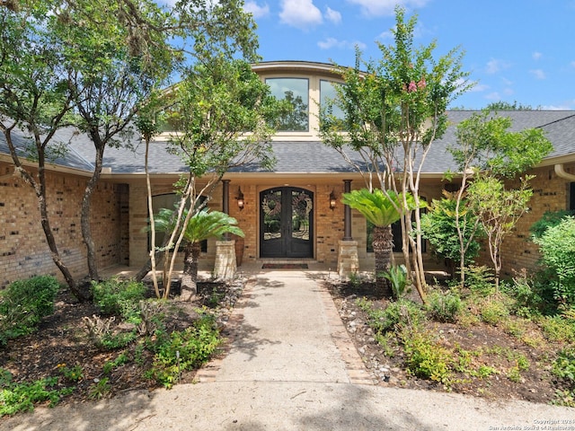 doorway to property with brick siding, french doors, and a shingled roof