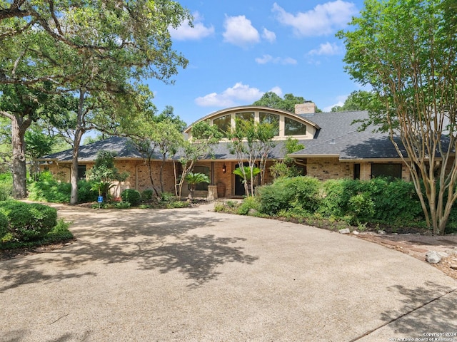 view of front of property featuring roof with shingles, a chimney, driveway, and brick siding
