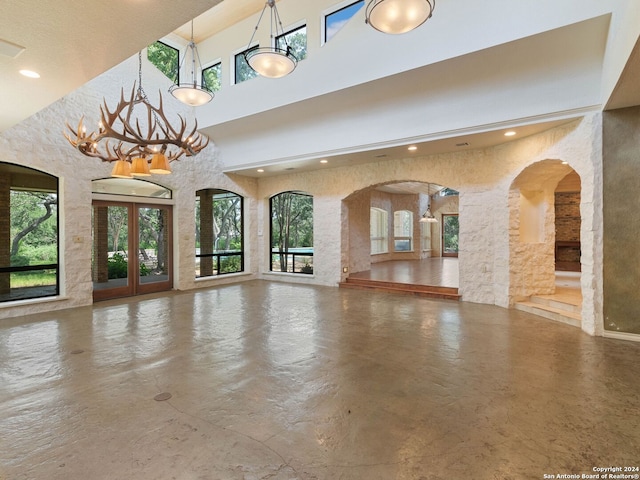 unfurnished living room featuring concrete floors, recessed lighting, arched walkways, and a towering ceiling