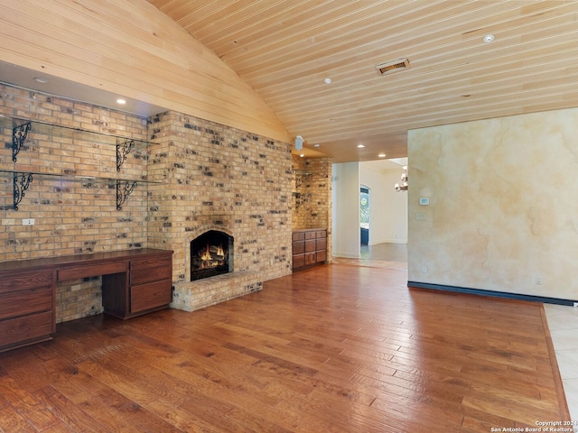 unfurnished living room with an inviting chandelier, a fireplace, visible vents, vaulted ceiling, and hardwood / wood-style flooring