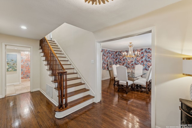 stairway with a textured ceiling, wood-type flooring, and a chandelier