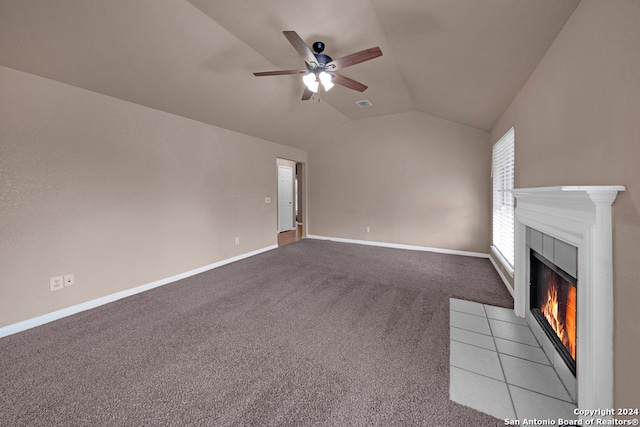 unfurnished living room with ceiling fan, a tile fireplace, light colored carpet, and vaulted ceiling