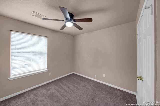 carpeted empty room with ceiling fan, plenty of natural light, and a textured ceiling