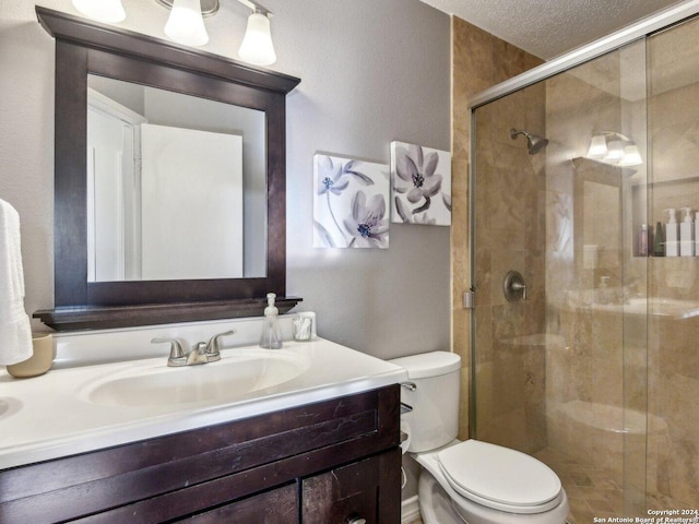 bathroom featuring a textured ceiling, vanity, toilet, and a shower with shower door