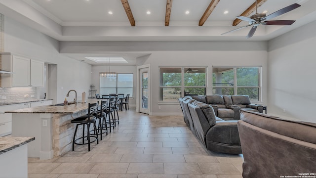 living room with sink, ceiling fan with notable chandelier, and beam ceiling