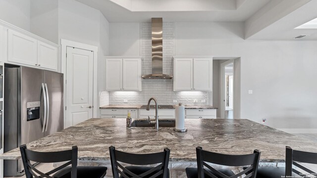 kitchen featuring an island with sink, stone counters, wall chimney range hood, and a kitchen bar