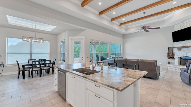 kitchen featuring a fireplace, ceiling fan with notable chandelier, white cabinetry, sink, and a kitchen island with sink