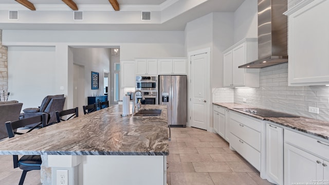 kitchen featuring dark stone countertops, a kitchen bar, stainless steel appliances, an island with sink, and wall chimney exhaust hood