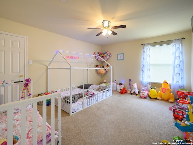 bedroom featuring a nursery area, ceiling fan, and carpet flooring