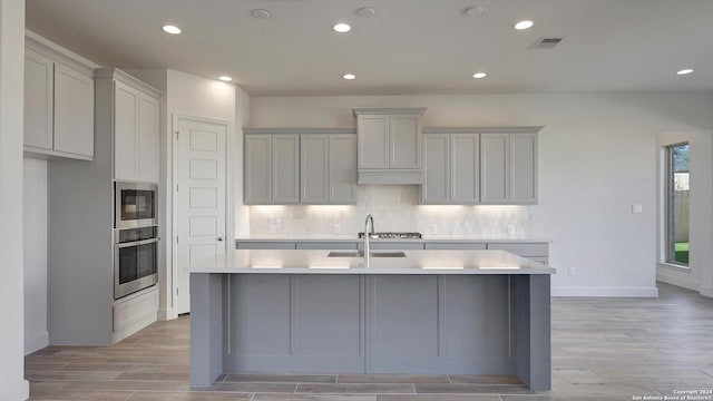 kitchen featuring tasteful backsplash, visible vents, appliances with stainless steel finishes, a kitchen island with sink, and a sink