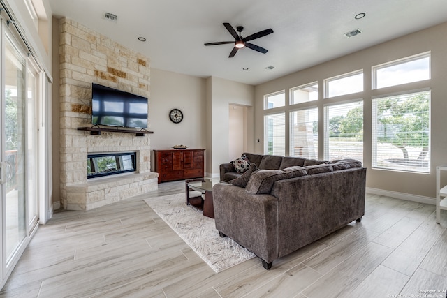 living room with ceiling fan, a stone fireplace, and light wood-type flooring