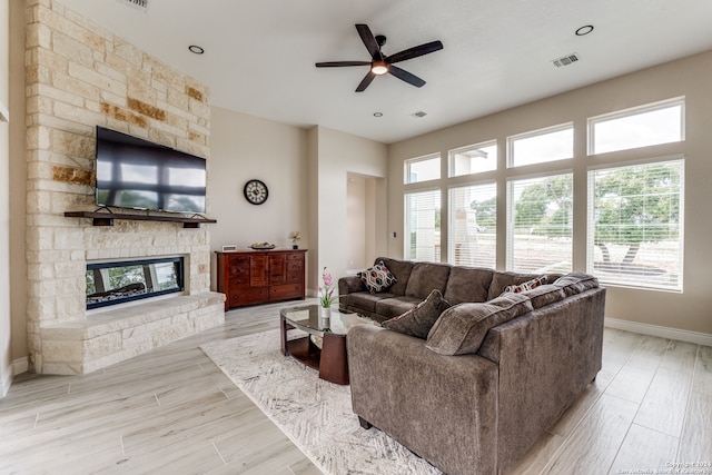 living room with light hardwood / wood-style flooring, ceiling fan, and a stone fireplace