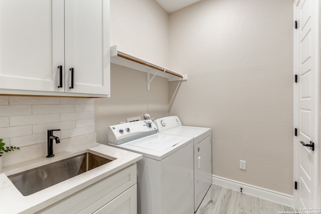 laundry area with cabinets, independent washer and dryer, sink, and light hardwood / wood-style floors