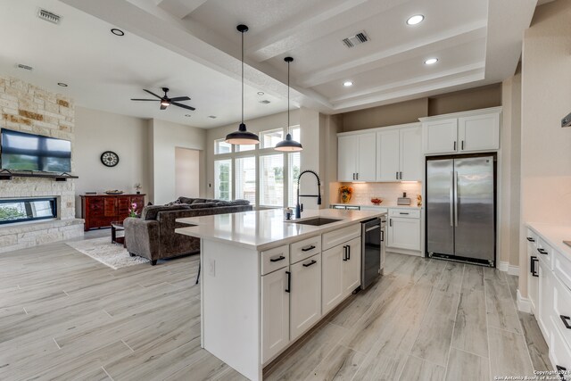 kitchen featuring a fireplace, stainless steel refrigerator, sink, ceiling fan, and a center island with sink