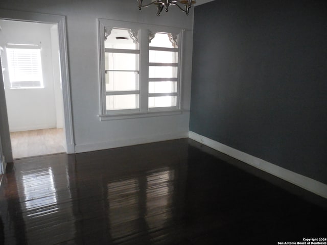 unfurnished room featuring dark wood-type flooring, plenty of natural light, and a notable chandelier