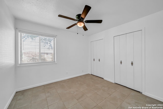 unfurnished bedroom featuring a textured ceiling, ceiling fan, light tile patterned floors, and two closets