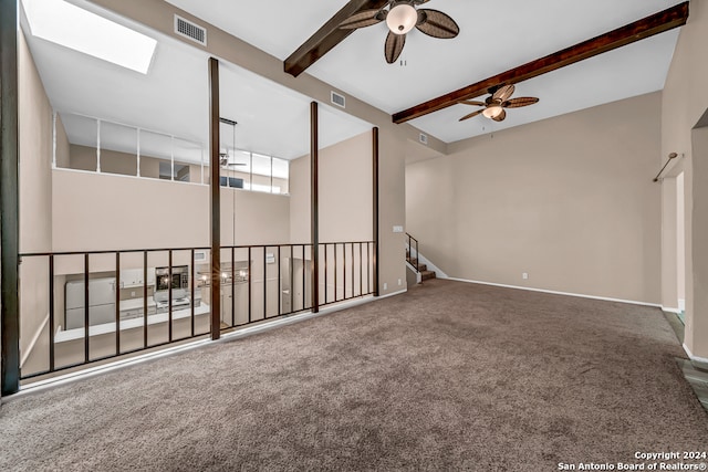 empty room featuring beamed ceiling, ceiling fan, carpet flooring, and a skylight