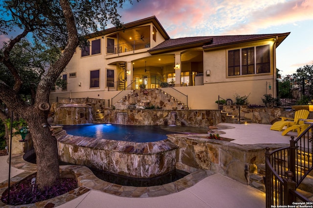 back of property at dusk featuring a balcony, stairway, a patio area, and stucco siding