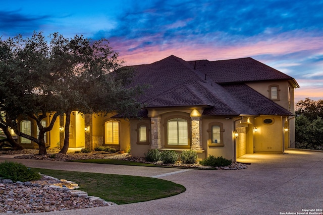 view of front of house featuring a shingled roof, curved driveway, and stucco siding