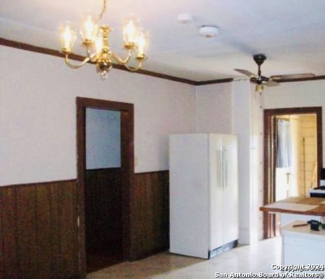 unfurnished dining area with wood walls, ceiling fan with notable chandelier, and ornamental molding