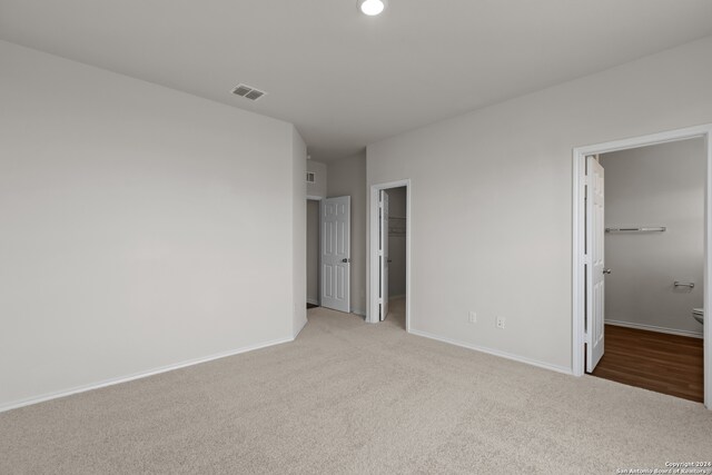 unfurnished bedroom featuring a closet, ensuite bath, a walk in closet, and light carpet