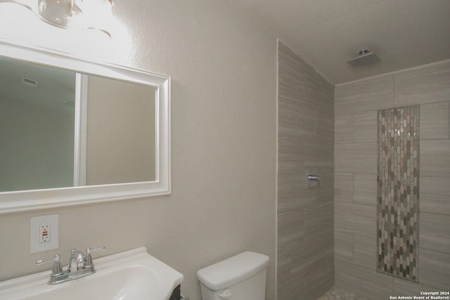 bathroom with toilet, tiled shower, and sink