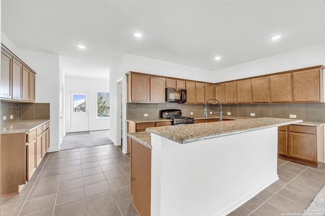 kitchen with light tile patterned floors, stainless steel gas range oven, light stone countertops, black microwave, and a sink