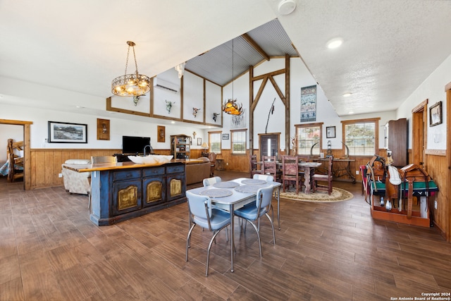 dining area featuring a textured ceiling, wood walls, dark hardwood / wood-style floors, a chandelier, and lofted ceiling with beams