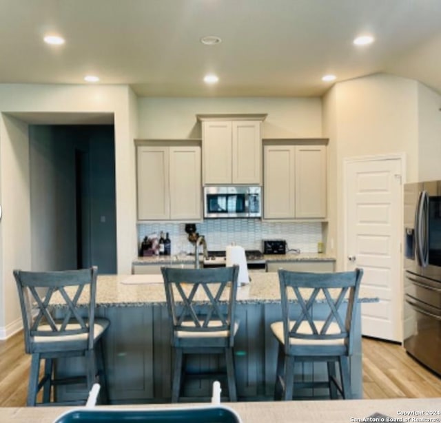 kitchen with a center island with sink, a breakfast bar area, light stone counters, and appliances with stainless steel finishes