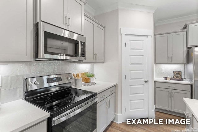 kitchen with appliances with stainless steel finishes, gray cabinetry, backsplash, wood-type flooring, and crown molding